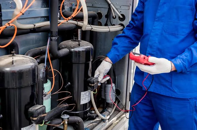 HVAC technician using diagnostic meters on compressor equipment